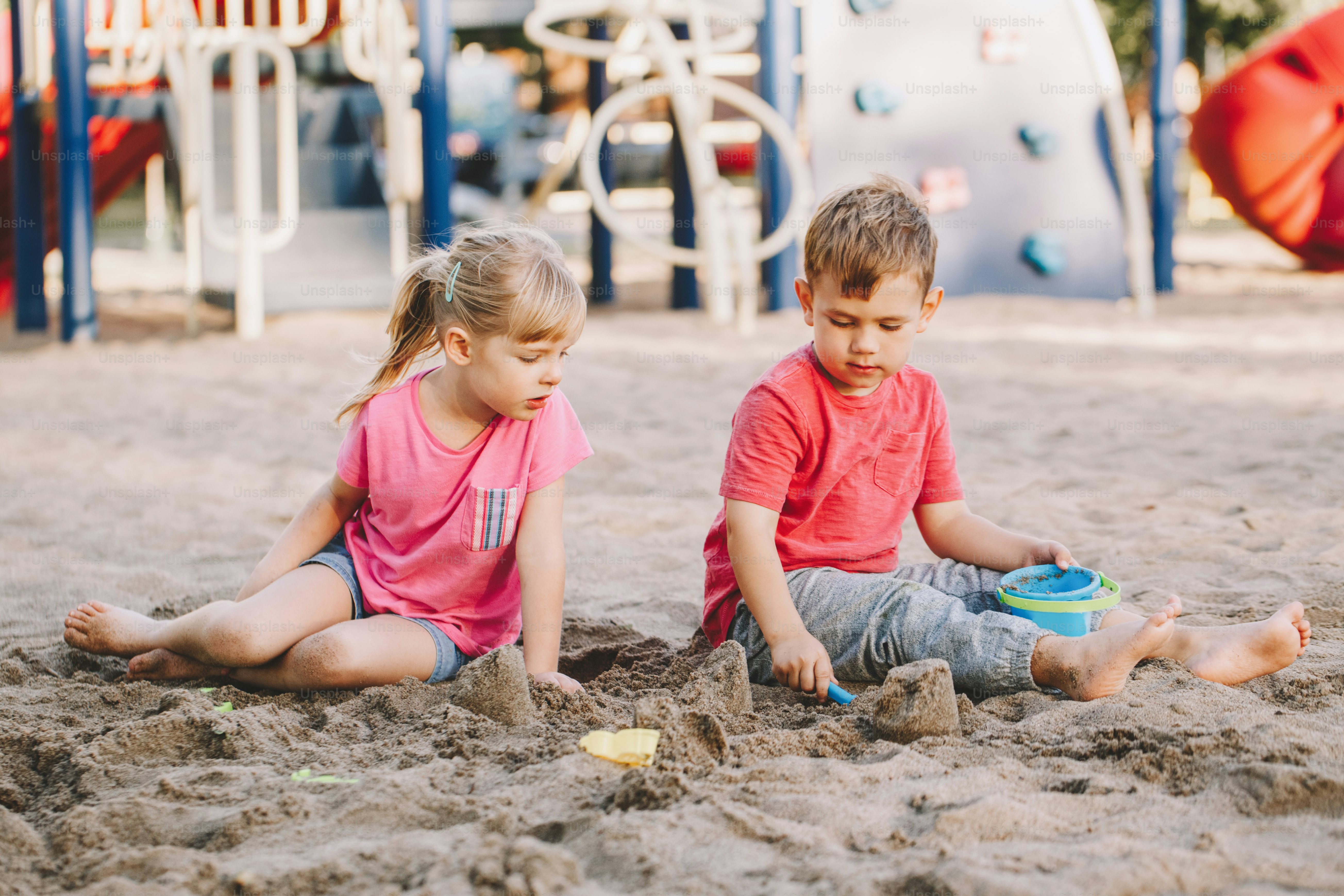 Dua anak Kaukasia duduk di kotak pasir bermain mainan pantai. Teman gadis dan laki-laki kecil bersenang-senang bersama di taman bermain. Aktivitas luar ruangan musim panas untuk anak-anak. Waktu luang, gaya hidup, masa kanak-kanak.
