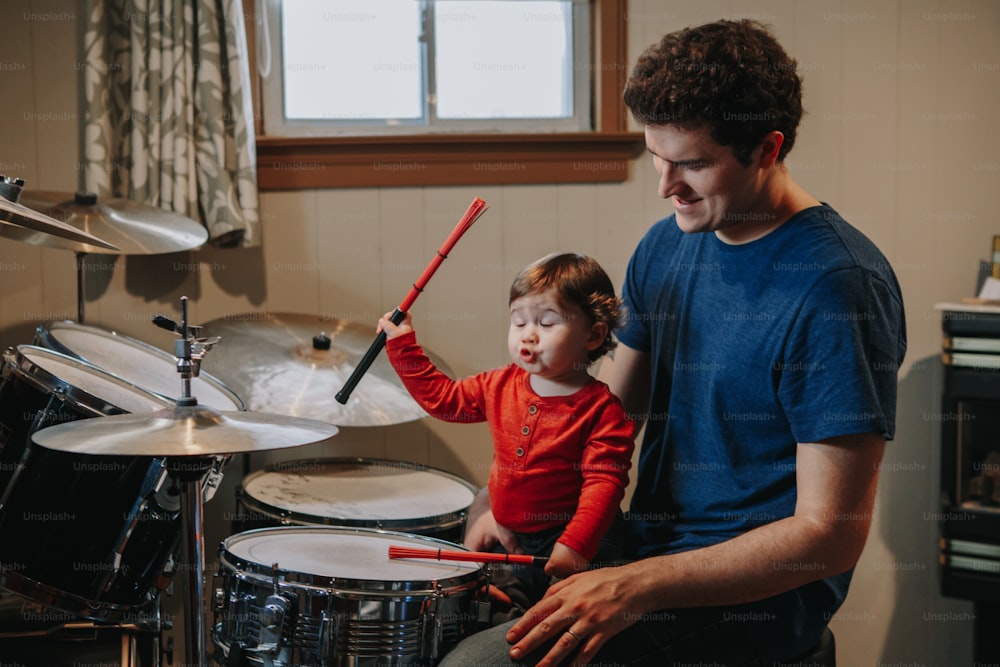 Father teaching baby boy to play drums. Parent with toddler child having fun and spending time together. Dad and kid playing music. Family hobby activity and leisure time.