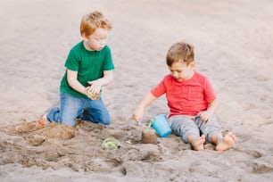 Two Caucasian children sitting in sandbox playing with beach toys. Little boys friends having fun together on playground. Summer outdoor activity for kids. Leisure time lifestyle childhood.