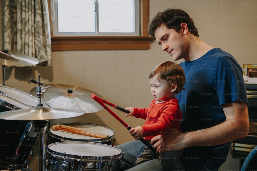 Padre che insegna al bambino a suonare la batteria. Genitore con bambino che si diverte e trascorre del tempo insieme. Papà e bambino che suonano musica. Attività hobby in famiglia e tempo libero.