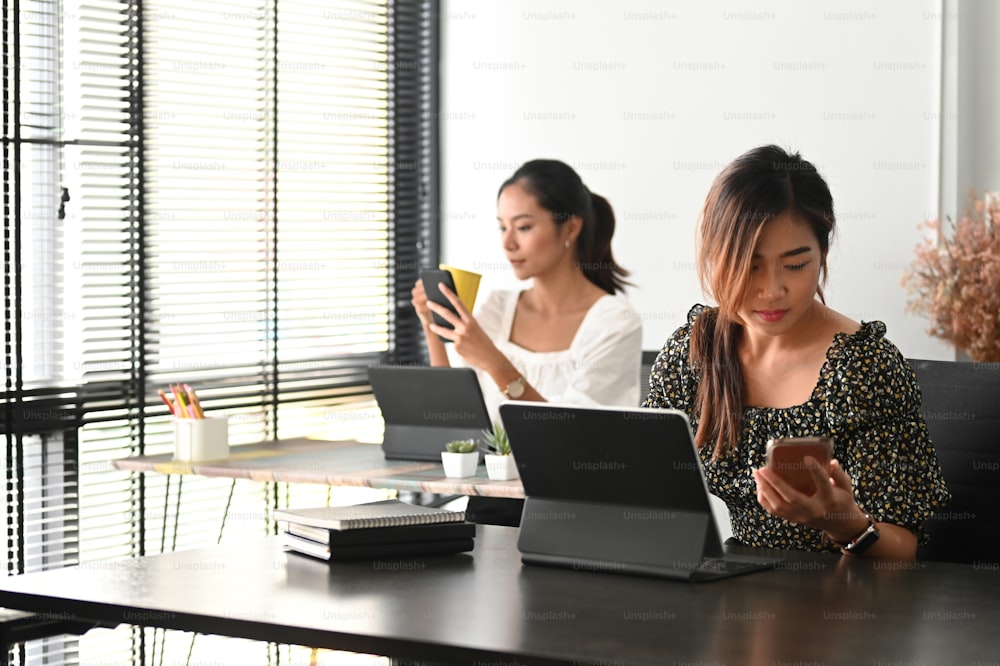 Mujer joven con ropa informal que trabaja en una tableta en el interior de la oficina moderna de la empresa emergente y su colega en el fondo.