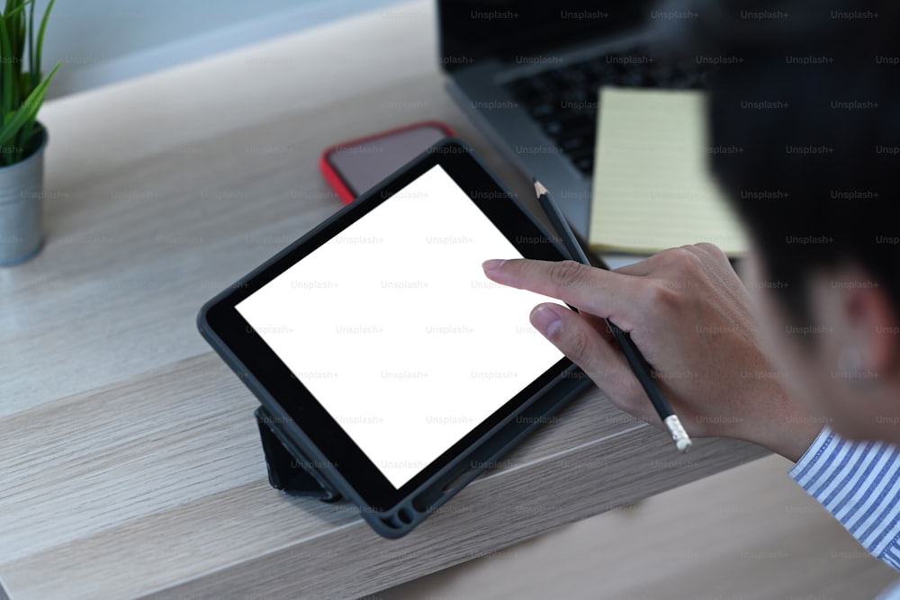 Um jovem freelancer tocando na tela do tablet digital enquanto trabalha em um novo projeto em casa.