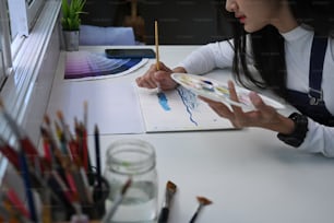 かなり才能のある女性画家が、クリエイティブなワークスペースで水彩絵の具で絵を描いている横から見た写真。