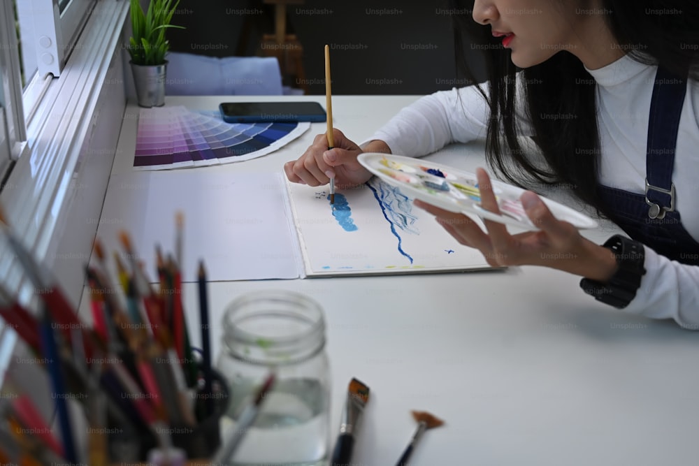 Vista lateral de uma pintora muito talentosa está pintando com tintas de aquarela em seu espaço de trabalho criativo.