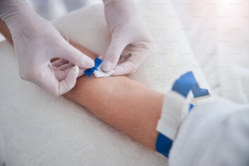 美容センターで患者のための治療ビタミン点滴を受ける手袋の看護師の手の接写