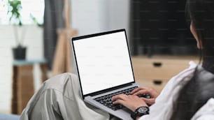 A young female relaxing on sofa and using laptop computer mock up blank white screen.