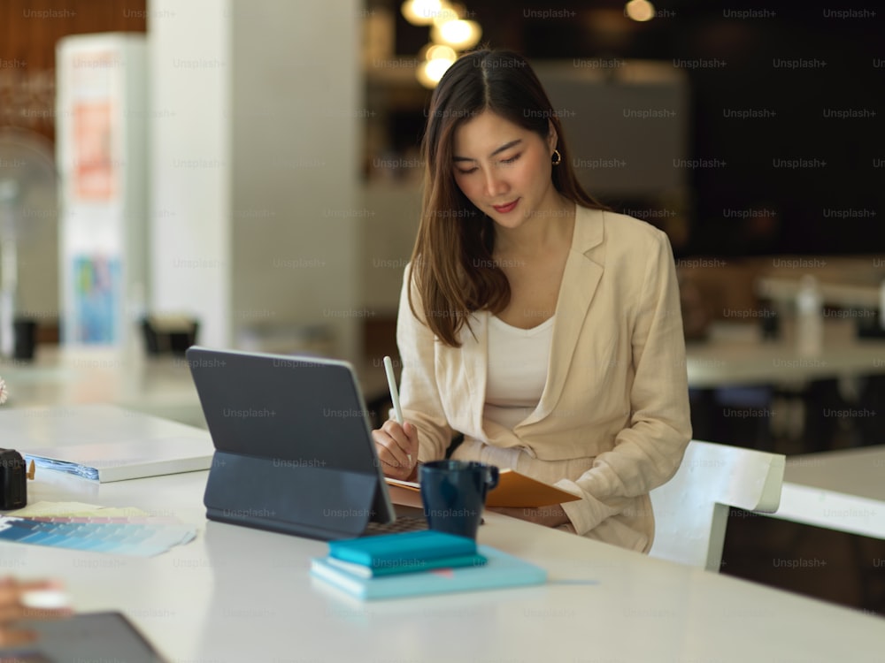 Ritratto di donna d'affari che lavora con libro di pianificazione e tablet sul tavolo da lavoro in caffetteria
