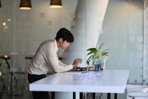 A male designer working on browsing information for project on computer laptop at office.