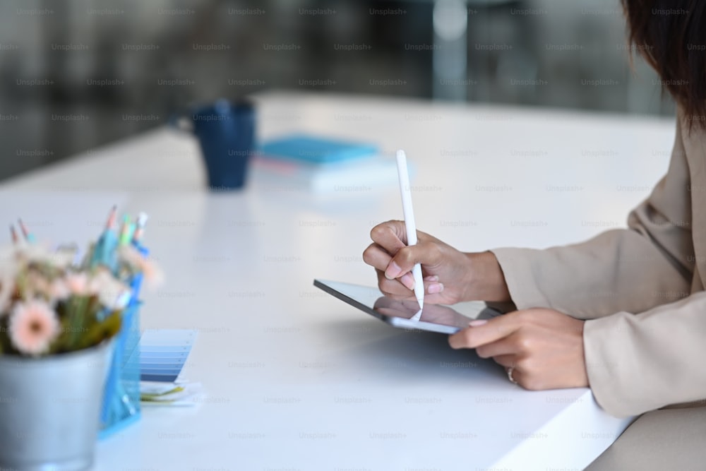 Plan recadré d’une femme designer créative utilisant une tablette avec un stylet travaillant sur un projet au bureau.