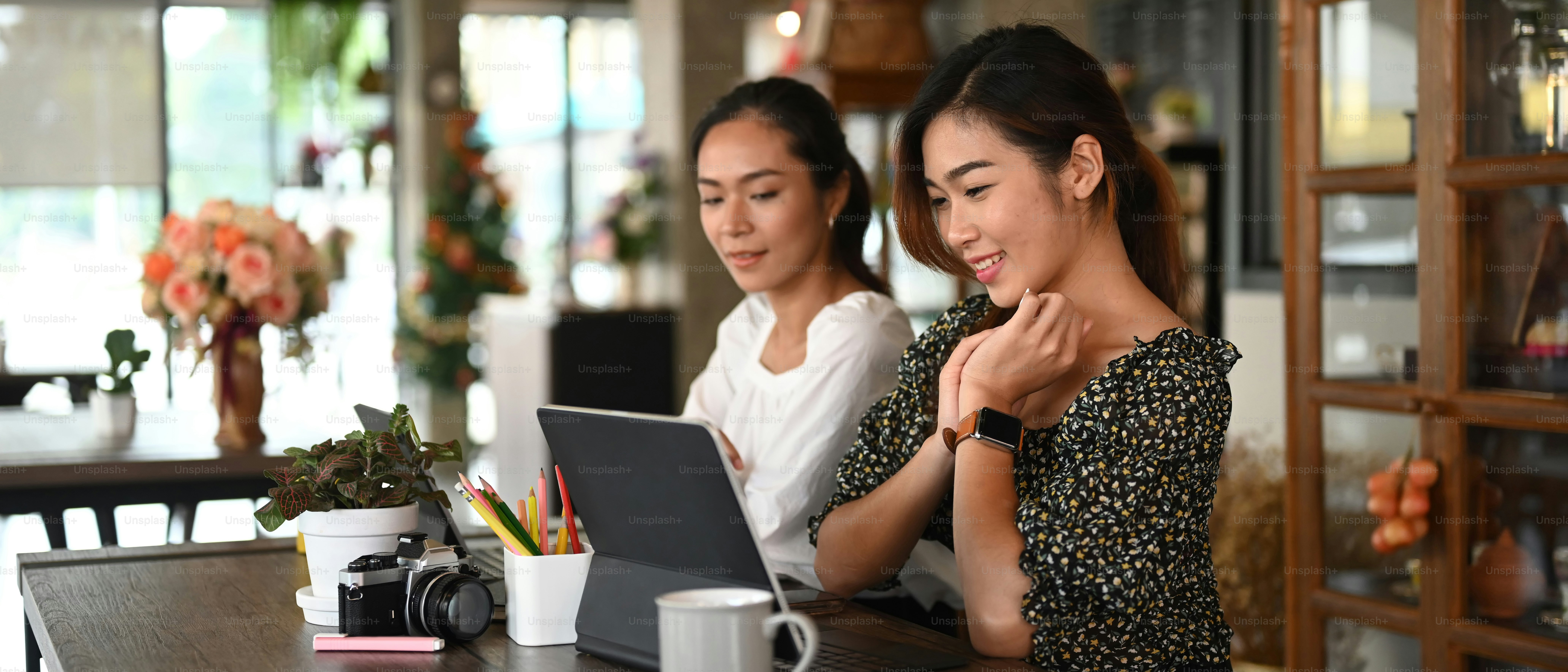 Zwei erfolgreiche Geschäftsfrauen diskutieren Projekt auf Tablet im modernen Büro.