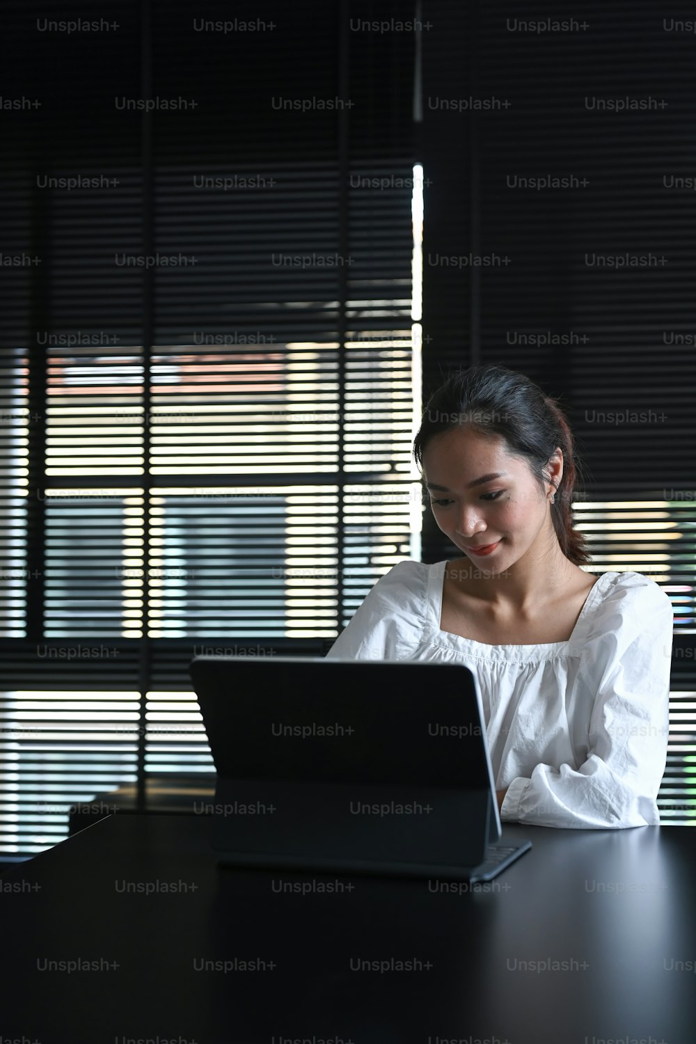 Mulher sorridente usando tablet de computador enquanto está sentada no escritório moderno.