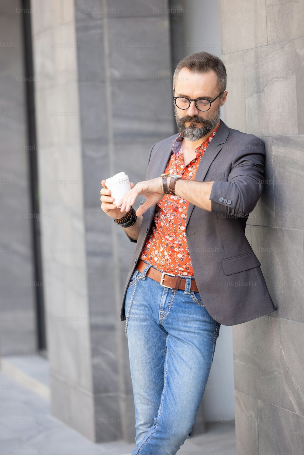 カジュアルな服を着たハンサムな男が街で誰かを待っている時間をチェックし、屋外でコーヒーを飲む男