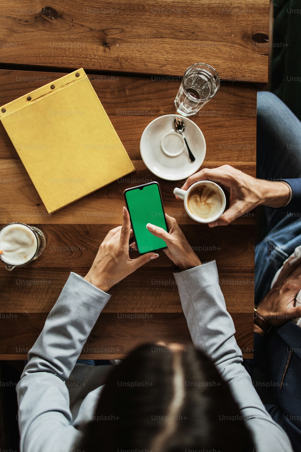 Imagen de maqueta de una gente de negocios sosteniendo un teléfono móvil inteligente con pantalla verde en blanco en una mesa de madera vintage en un restaurante de café moderno durante la reunión o el almuerzo.