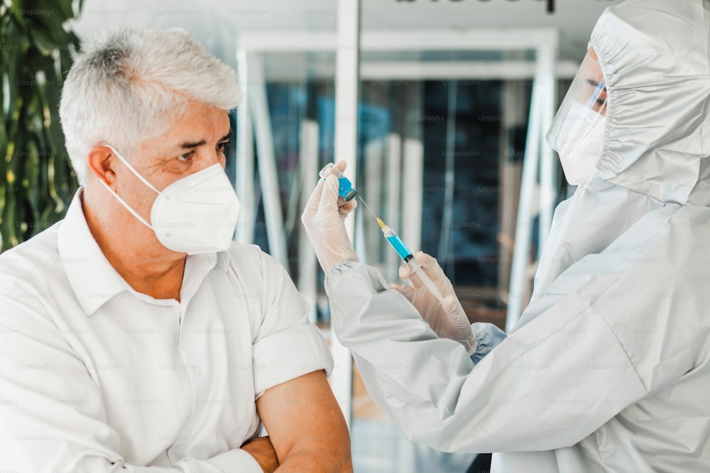 vecchio uomo latino che riceve il colpo del vaccino per una donna medica messicana con la maschera facciale per la pandemia di coronavirus a Città del Messico