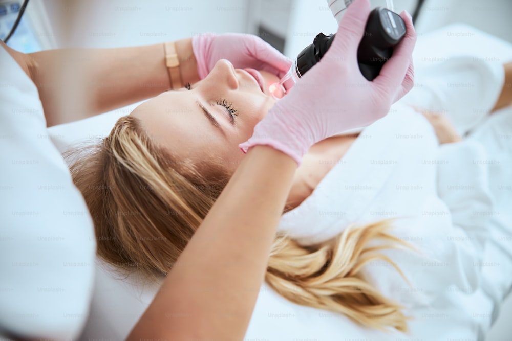 Paciente loira caucasiana jovem atraente deitada com os olhos fechados durante um procedimento cosmético