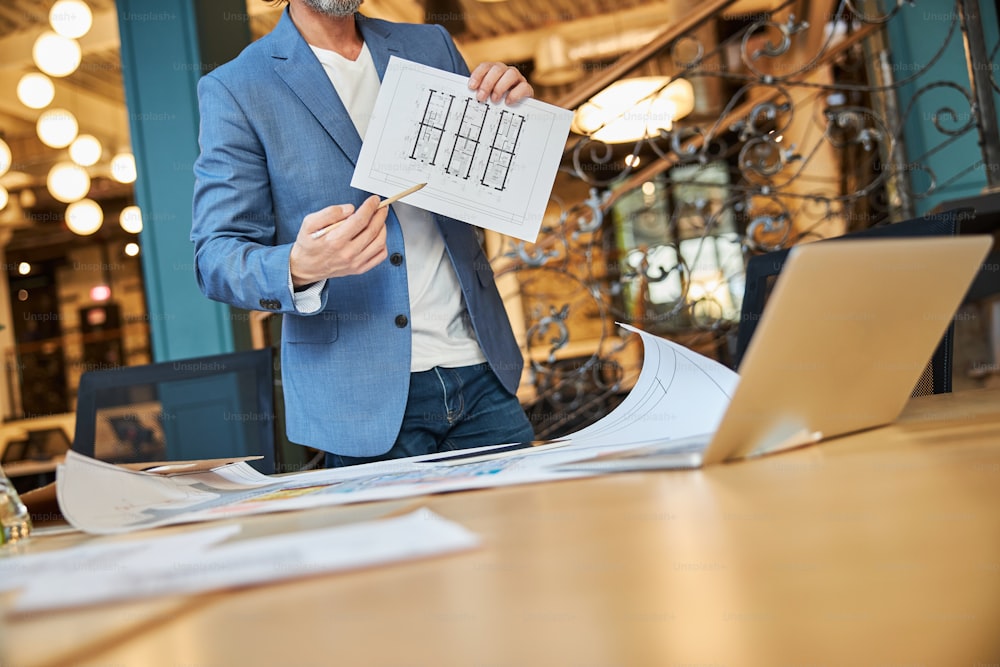 Cropped photo of man in blazer pointing to a schematic picture while having a video-call