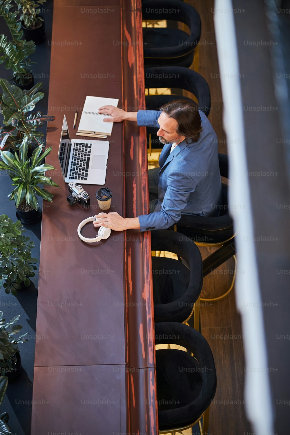 Foto de la vista superior de un hombre de negocios enfocado colocando una computadora portátil y otros dispositivos en una mesa en el salón del hotel