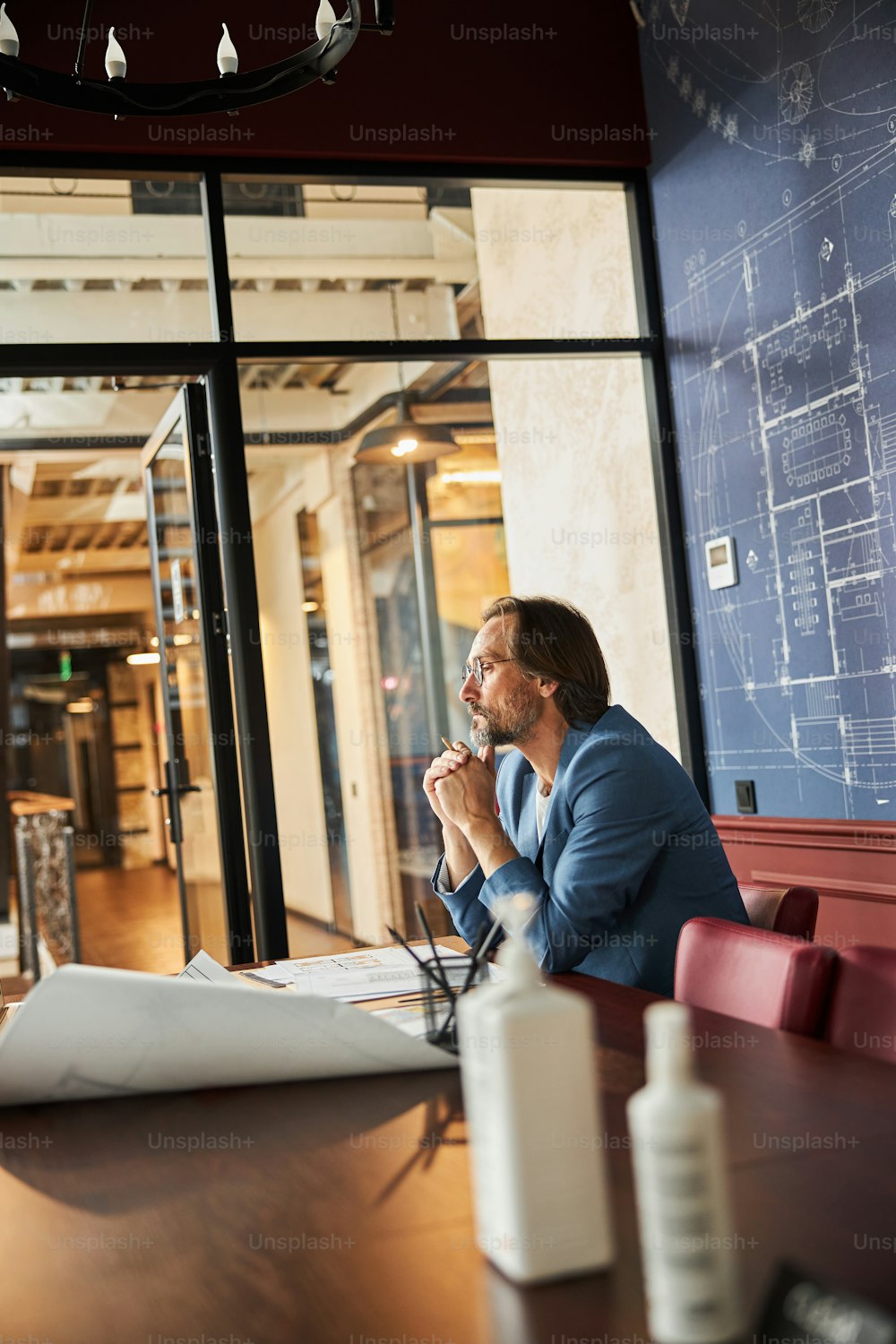 Serious man in smart blazer looking thoughtful while sitting at a long wooden table