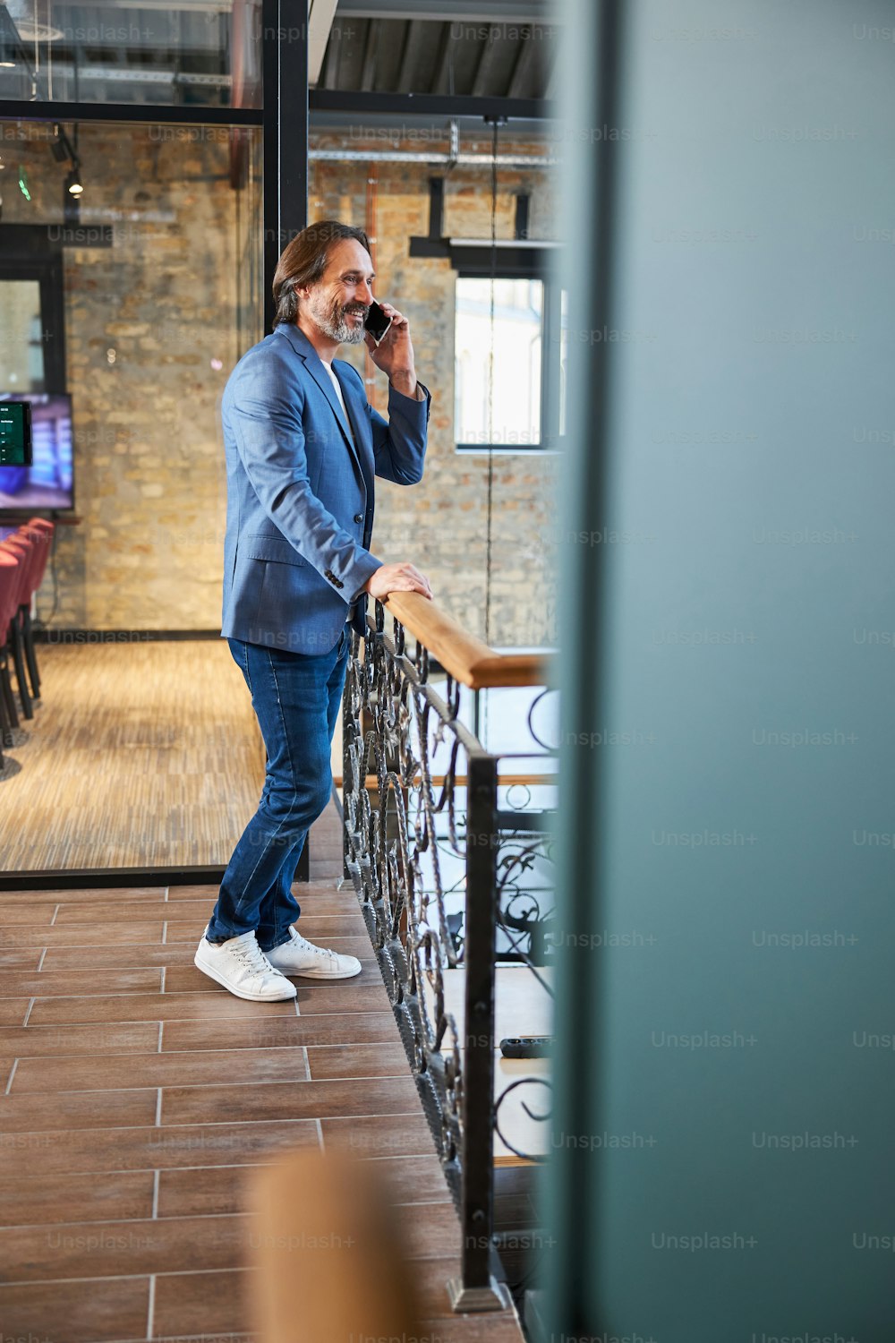 Full-length copy space photo of smiley brunette man in blue jacket talking on the phone in hotel hallway