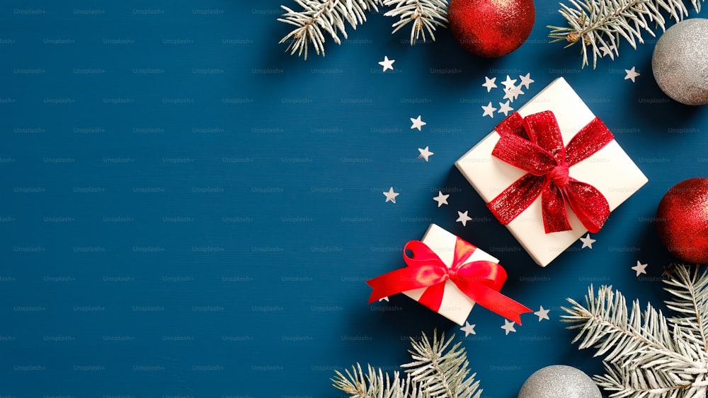 紙吹雪と濃紺の背景に赤いリボンの弓、ボールの装飾、松の木の枝と白いギフトボックス。クリスマスプレゼントのコンセプト。フラットレイ、上面図。