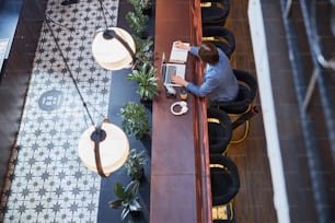 Responsible adult taking notes while sitting at the bar counter and working remotely from hotel