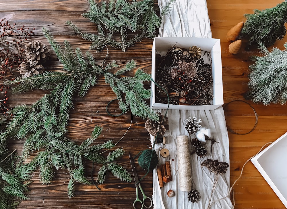 木製の素朴なテーブルの上面図に松ぼっくり、はさみ、糸、果実でクリスマスの素朴なリースを作ります。お祝いの家の装飾。ハッピーホリデーとメリークリスマス!