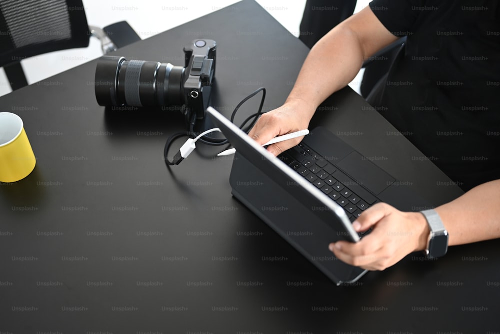 Plan recadré d’un photographe masculin en train de retoucher des photos avec une tablette d’ordinateur dans son espace de travail créatif.