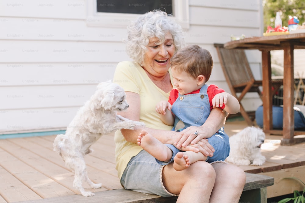 Grandmother sitting with grandson boy on porch at home backyard. Bonding of relatives and generation communication. Old woman with baby having fun spending time together outdoor.