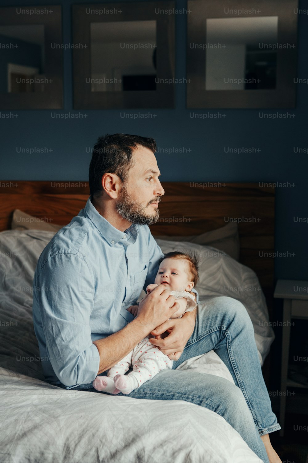 膝の上に揺れる新生児を抱える中年の白人の父。疲れた男の親は、腕の手に子供と家のベッドに座っています。本物のライフスタイルの家族の瞬間。シングルパパの家庭生活のコンセプト。