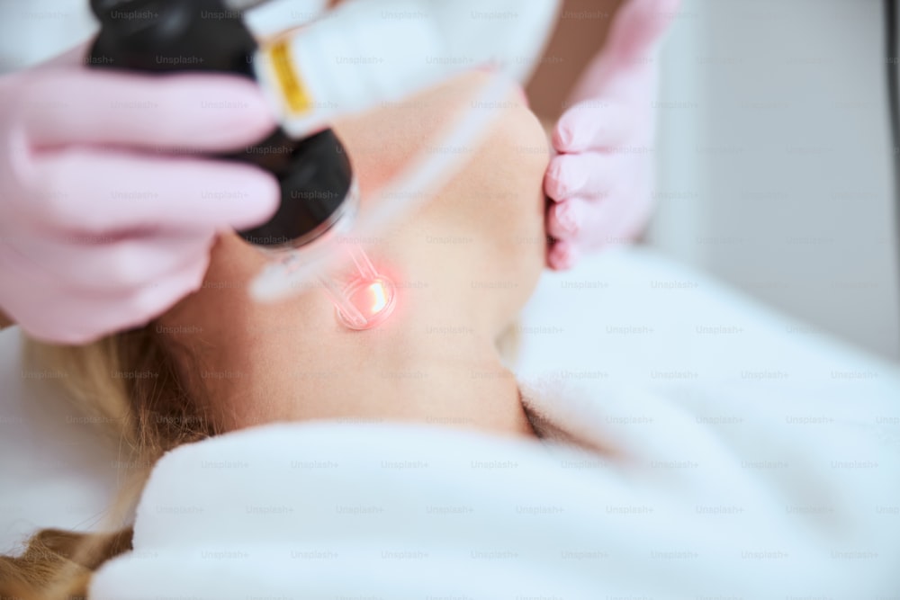 Cropped photo of a qualified dermatologist in latex gloves performing a fractional laser resurfacing procedure