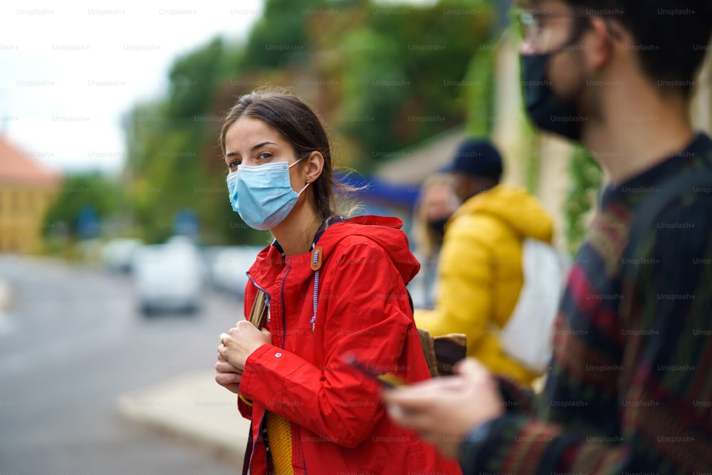 Young people on bus stop outdoors in town. Coronavirus and safe distance concept.