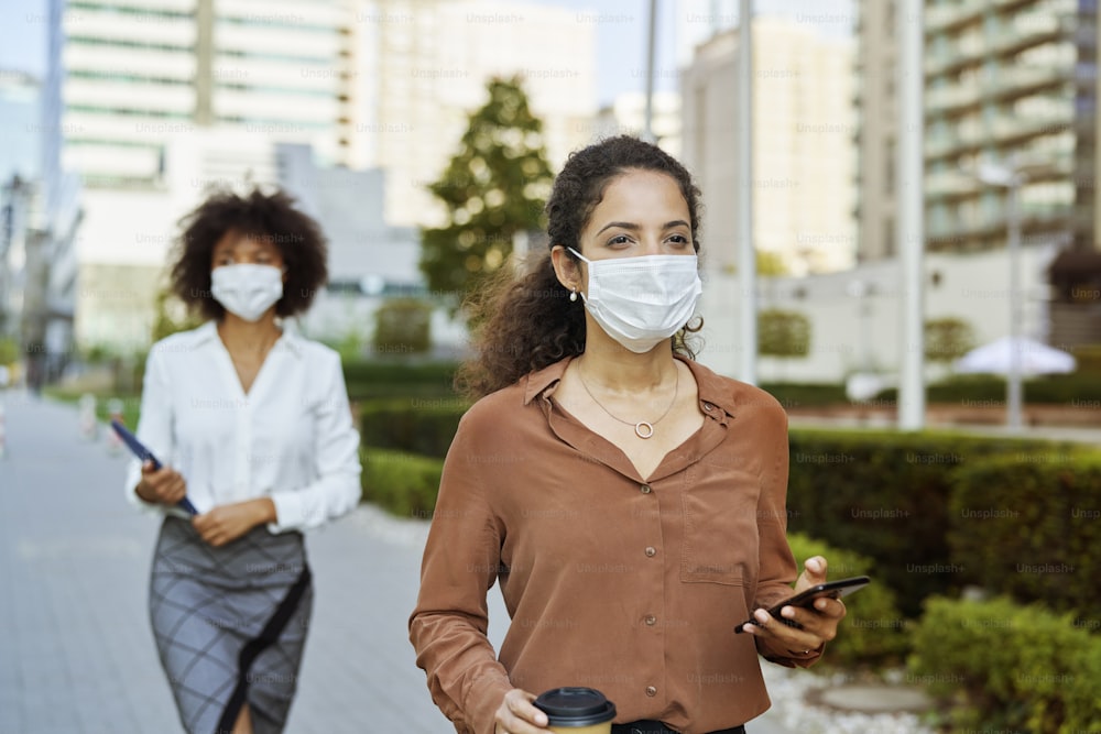 Geschäftsfrauen, die in schützenden Gesichtsmasken durch die Stadt gehen