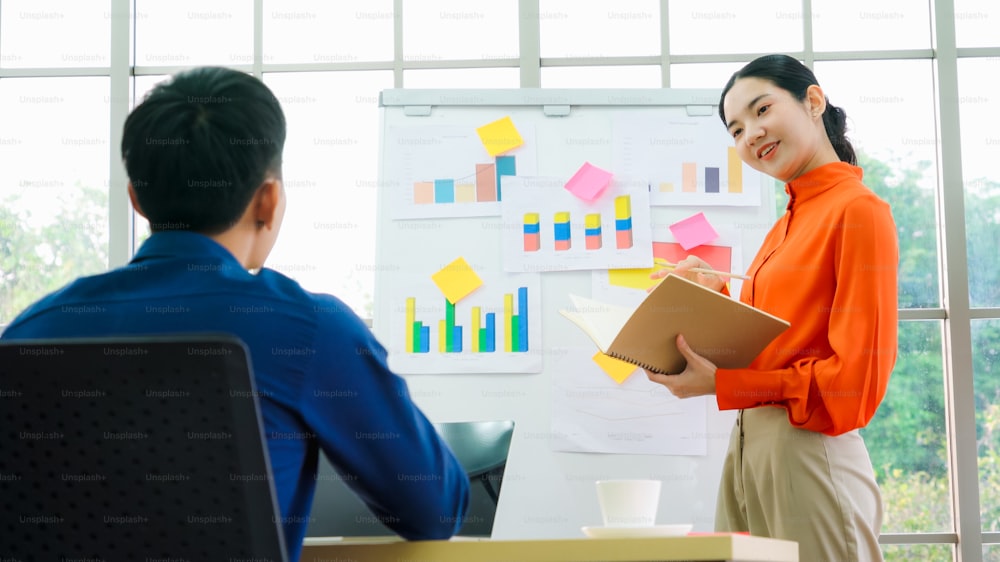 Mujer joven explica los datos de negocios en la pizarra blanca en la sala de oficina informal. La empresaria asiática segura de sí misma informa sobre el progreso de la información de un proyecto empresarial para asociarse para determinar la estrategia de mercado.