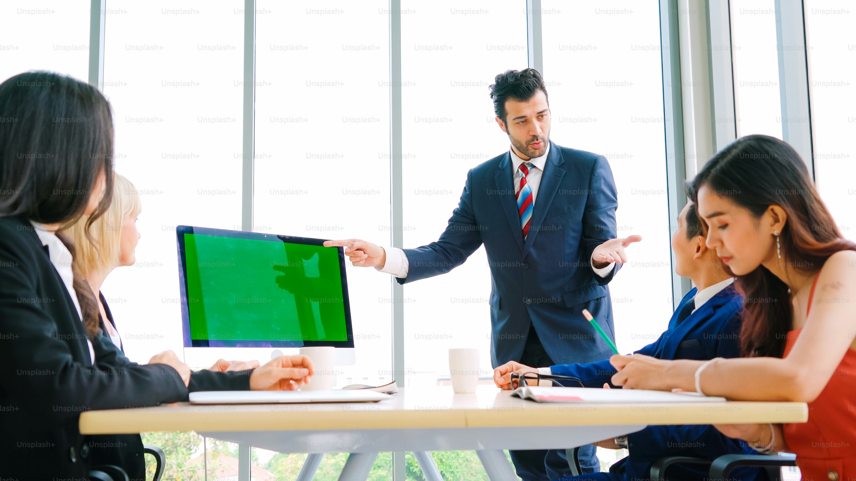 Business people in the conference room with green screen chroma key TV or computer on the office table. Diverse group of businessman and businesswoman in meeting on video conference call .