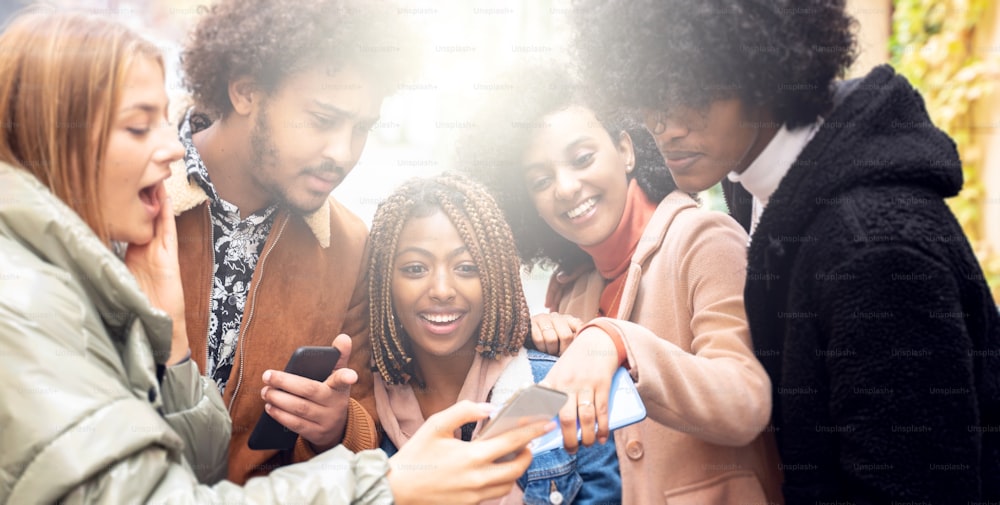 Group Of Laughing Friends looking at social media on mobile phone, laughing, spending funny time together. Multi ethnic friendship concept.