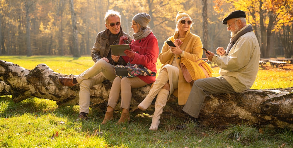 Des personnes âgées utilisant des téléphones intelligents mobiles et des tablettes dans un magnifique parc d’automne. Des amis retraités qui passent du temps ensemble à l’extérieur.