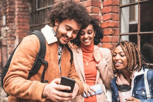 Three young african friends watching funny things on social media on mobile phone, smiling and having fun. Outdoor photo. Afro people spending time together. Lifestyle concept.