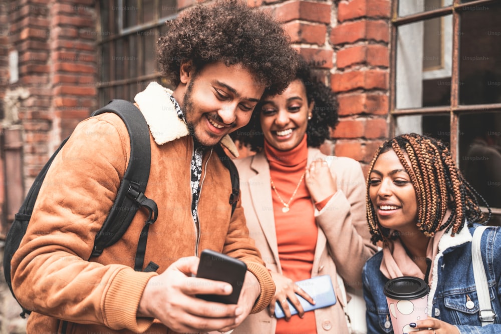 Três jovens amigos africanos assistindo coisas engraçadas nas mídias sociais no celular, sorrindo e se divertindo. Foto ao ar livre. Pessoas afro passando tempo juntas. Conceito de estilo de vida.