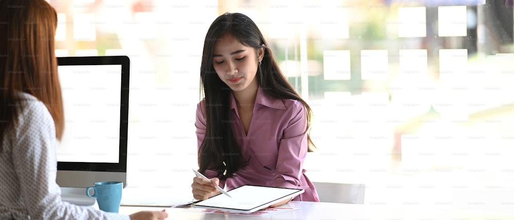 Foto de una mujer de negocios usando una tableta que presenta y discute un nuevo concepto de negocio con su colega en la oficina.