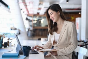 A beautiful businesswoman working on computer tablet and making notes in personal paper planner at desk.