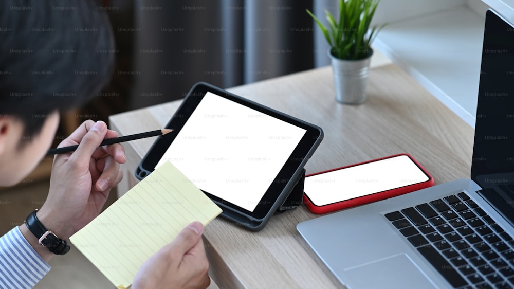 Cropped shot of man working with tablet and making notes in personal paper at desk.