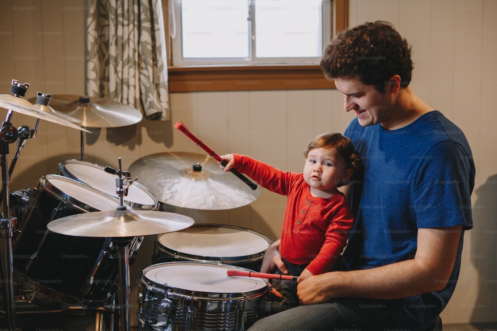 Padre enseñando a su bebé a tocar la batería. Padre con niño pequeño divirtiéndose y pasando tiempo juntos. Papá y niño tocando música. Actividad de pasatiempo familiar y tiempo libre.