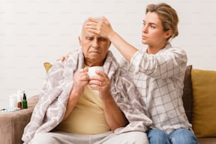 Mujer joven cuidando a su abuelo anciano con un síntoma de resfriado en casa