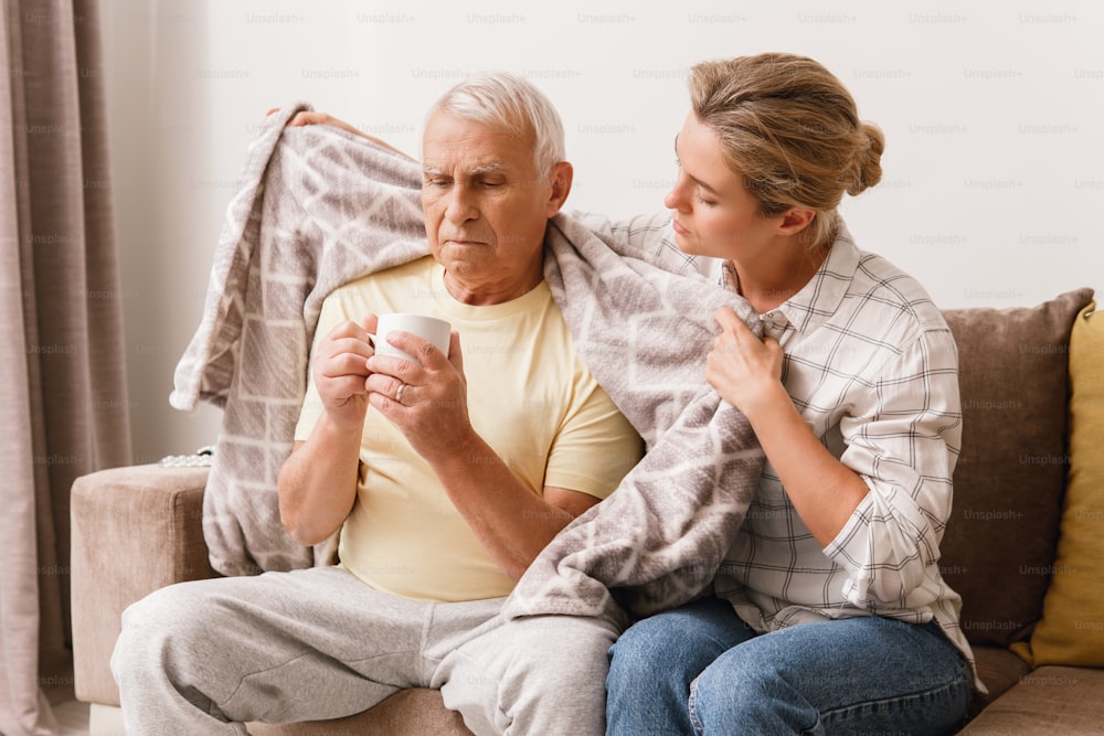 Young woman taking care of her elderly grandfather with a cold syptoms at home