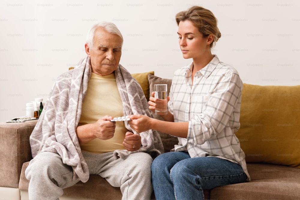 Young woman is giving medicine to her sick elderly grandfather at home