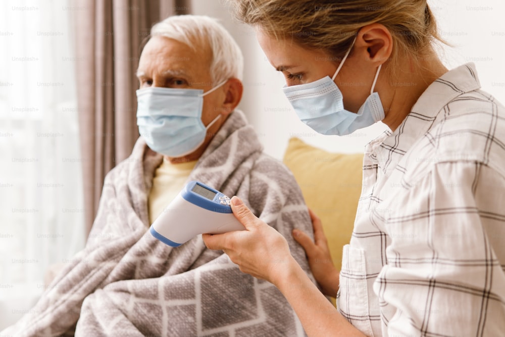 Mujer joven cuidando a su abuelo anciano con síntomas de resfriado en casa