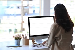 現代のオフィスでコンピューターを操作する若い女性従業員の後ろ姿。製品モンタージュの空白の画面。