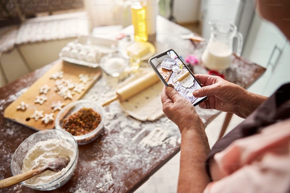 Photo recadrée d’une personne en tablier prenant une photo du processus de fabrication de la pâte sur le smartphone