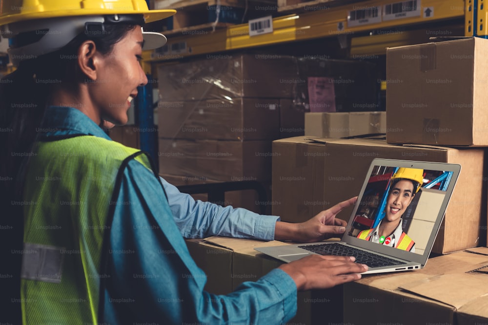 Warehouse staff talking on video call at computer screen in storage warehouse . Online software technology connects people working in logistic factory by virtual conference call on internet network .