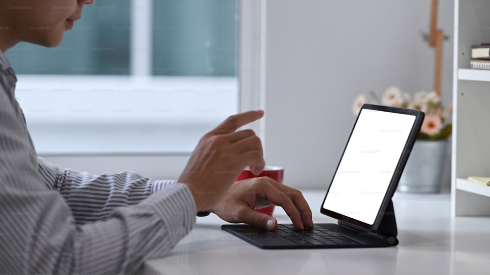 Vista lateral do freelancer masculino trabalhando em tablet de computador no local de trabalho moderno.